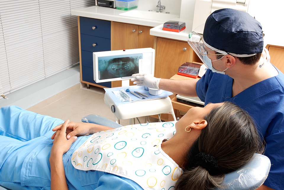 Kobieta leżąca u dentysty z założonym śliniakiem ogląda rentgen zgryzu, który pokazuje jej dentysta