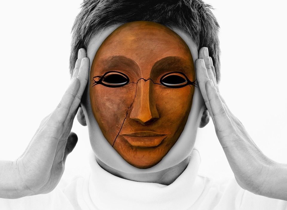 Gliniana popękana maska z namalowanymi konturami wokół oczu konturami na twarzy człowieka, który trzyma się z skronie.