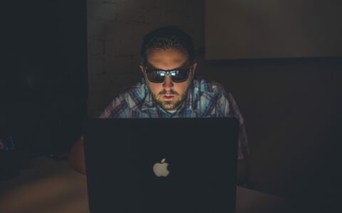 mężczyzna przy komputerze w ciemnym pokoju, w ciemnych okularach