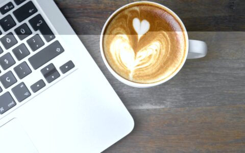 cappuccino z ładnym wzorem z pianki po prawej stronie kawałka laptopa