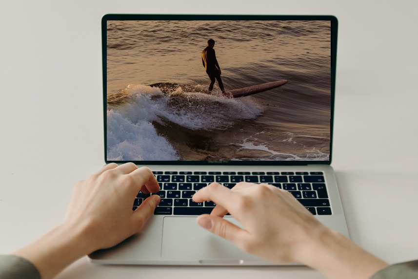 surfer na ekranie otwartego laptopa, na klawiaturze czyjeś dłonie