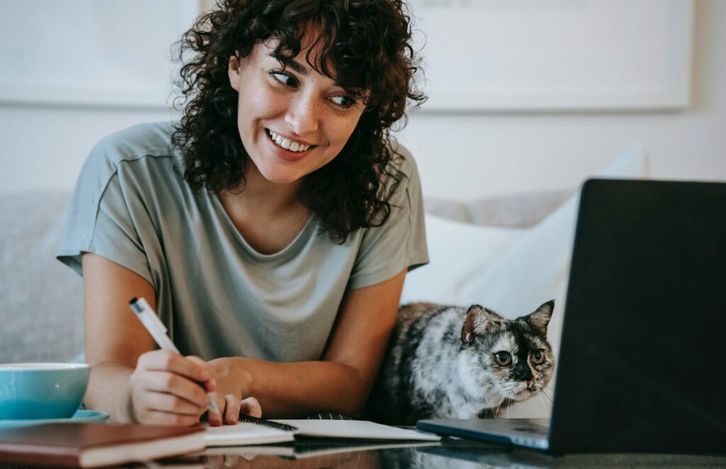młoda uśmiechnięta kobieta przed ekranem laptopa, obok niej siedzi kot
