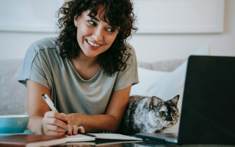 młoda uśmiechnięta kobieta przed ekranem laptopa, obok niej siedzi kot